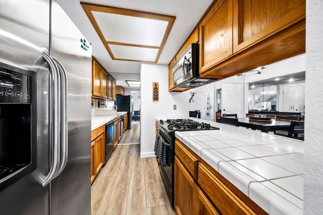 kitchen featuring tile countertops, black appliances, brown cabinets, and light wood finished floors