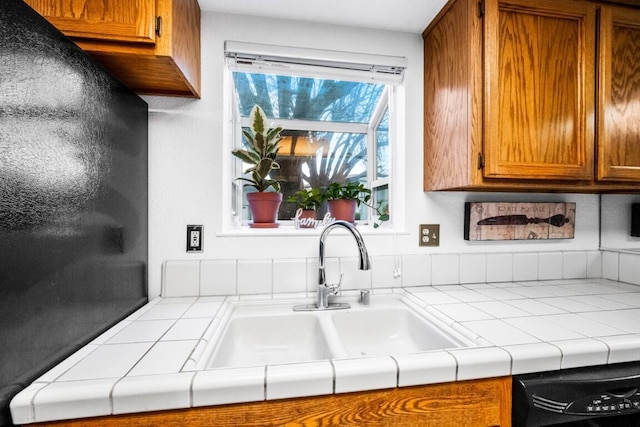 kitchen featuring tile countertops, brown cabinetry, a sink, and dishwasher