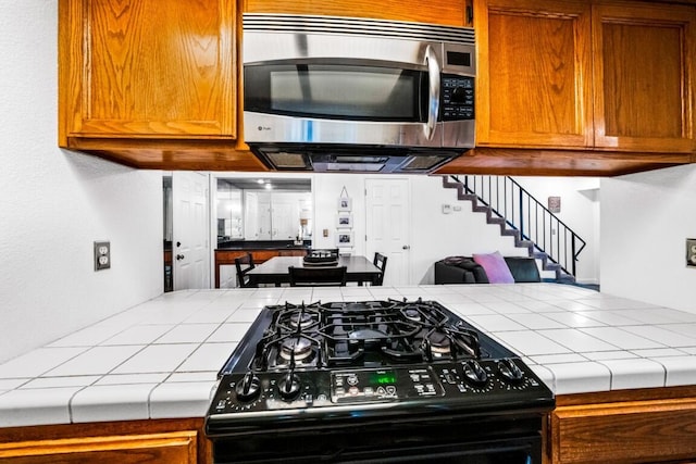 kitchen with brown cabinets, stainless steel microwave, black range with gas cooktop, and tile countertops