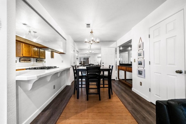 dining room featuring dark wood-style flooring, visible vents, a notable chandelier, and baseboards