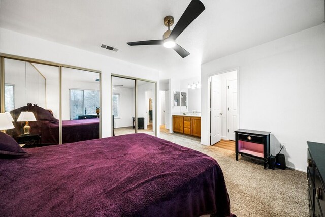 bedroom featuring two closets, visible vents, a ceiling fan, light carpet, and a sink