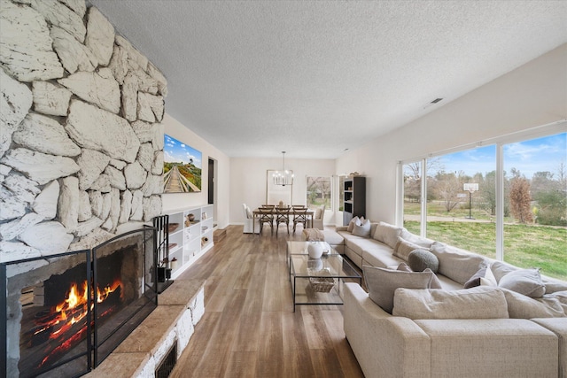 living room featuring a textured ceiling, a fireplace, wood finished floors, visible vents, and an inviting chandelier