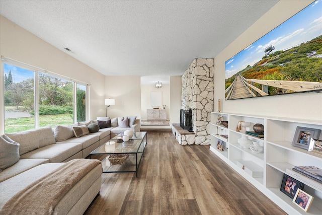 living room with a textured ceiling, wood finished floors, and a stone fireplace