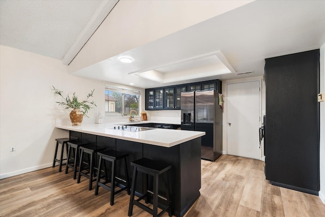 kitchen with a peninsula, a breakfast bar, light countertops, stainless steel refrigerator with ice dispenser, and glass insert cabinets