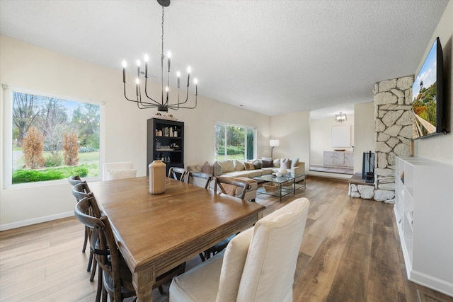 dining space with a textured ceiling, light wood finished floors, an inviting chandelier, and baseboards