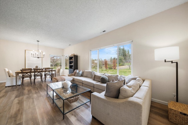 living room featuring a textured ceiling, dark wood-style flooring, visible vents, baseboards, and an inviting chandelier