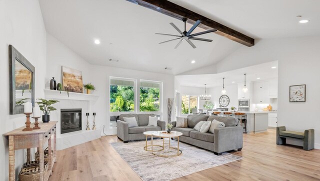 living area featuring high vaulted ceiling, light wood-style flooring, a premium fireplace, visible vents, and beam ceiling