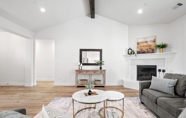 living room with vaulted ceiling with beams, light wood finished floors, a high end fireplace, and visible vents