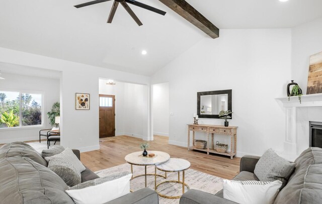 living area with ceiling fan, baseboards, beam ceiling, light wood finished floors, and a tiled fireplace