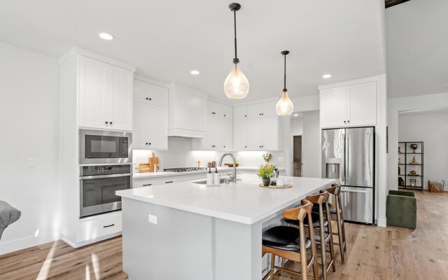 kitchen with a kitchen island with sink, stainless steel appliances, a sink, white cabinets, and light countertops