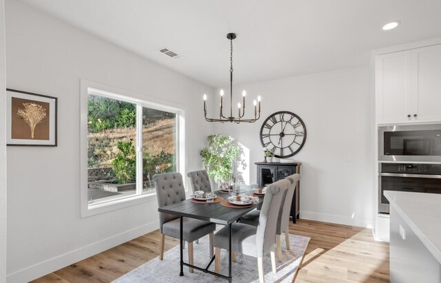 dining area with light wood-style flooring, visible vents, a chandelier, and baseboards