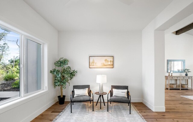 living area with light wood-style floors, baseboards, and beamed ceiling