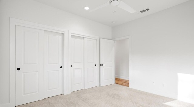 unfurnished bedroom featuring baseboards, visible vents, light colored carpet, two closets, and recessed lighting