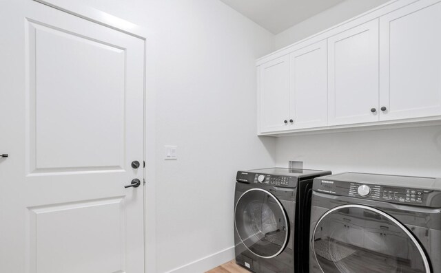 washroom featuring cabinet space, baseboards, light wood finished floors, and washing machine and clothes dryer