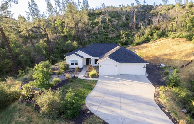 view of front of property featuring driveway, a shingled roof, an attached garage, and a view of trees