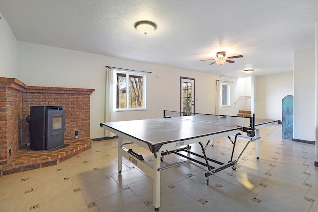 rec room with arched walkways, a wood stove, ceiling fan, a textured ceiling, and baseboards