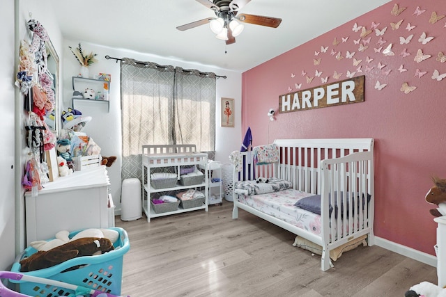 bedroom featuring a crib, baseboards, a ceiling fan, and wood finished floors