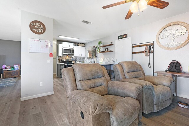 living area featuring ceiling fan, light wood finished floors, visible vents, and baseboards