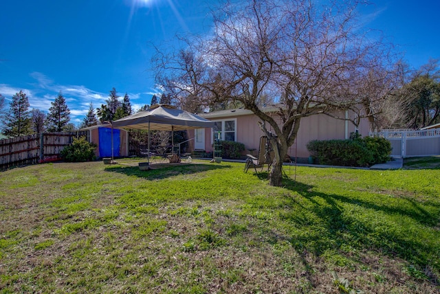 back of house featuring a storage shed, a lawn, a fenced backyard, a gazebo, and an outdoor structure