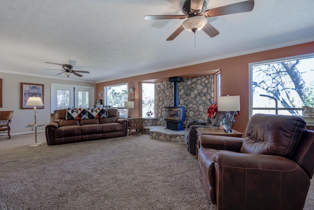 living room featuring ceiling fan, carpet floors, baseboards, a wood stove, and crown molding