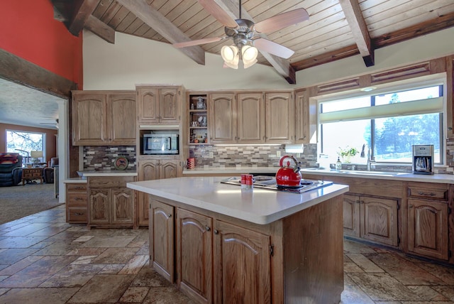 kitchen with stone tile floors, a kitchen island, stainless steel microwave, and light countertops