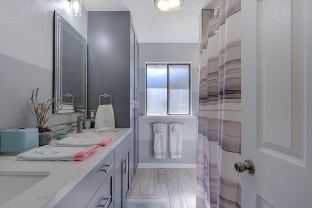 bathroom featuring double vanity, visible vents, baseboards, wood finished floors, and a sink