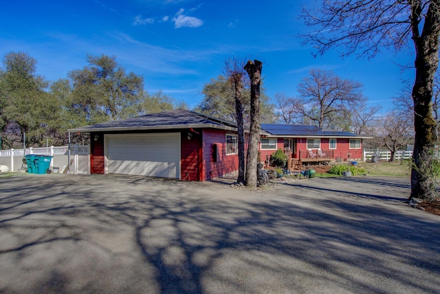 ranch-style house featuring an attached garage, fence, aphalt driveway, and solar panels