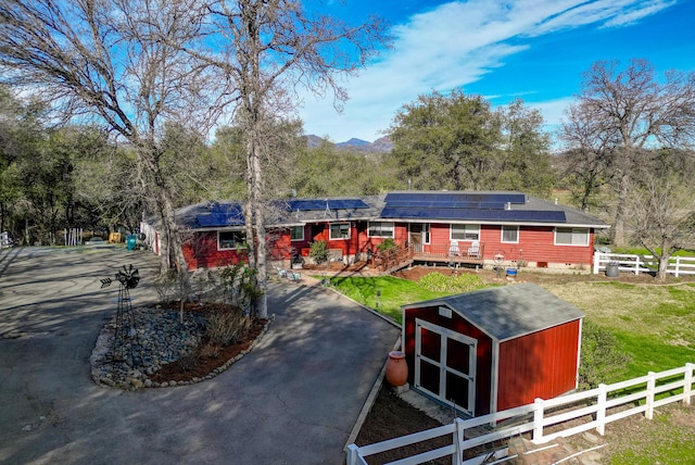 exterior space with aphalt driveway, fence private yard, an outdoor structure, roof mounted solar panels, and a front yard