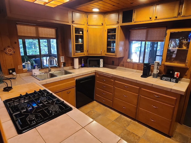 kitchen featuring tile counters, brown cabinetry, dishwasher, and a sink