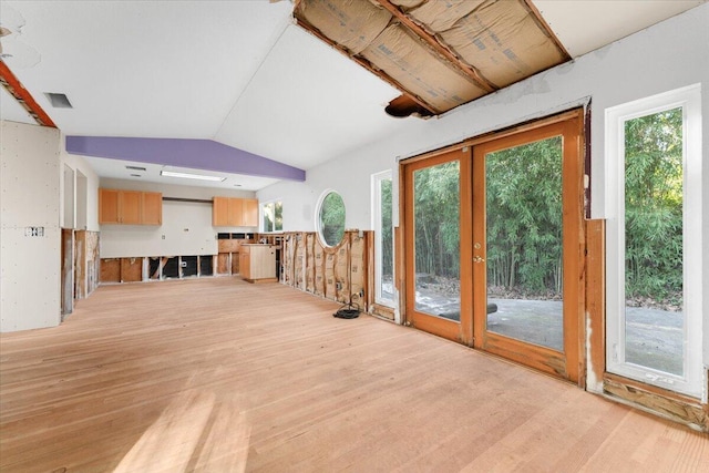 unfurnished living room with light wood finished floors, vaulted ceiling, and french doors