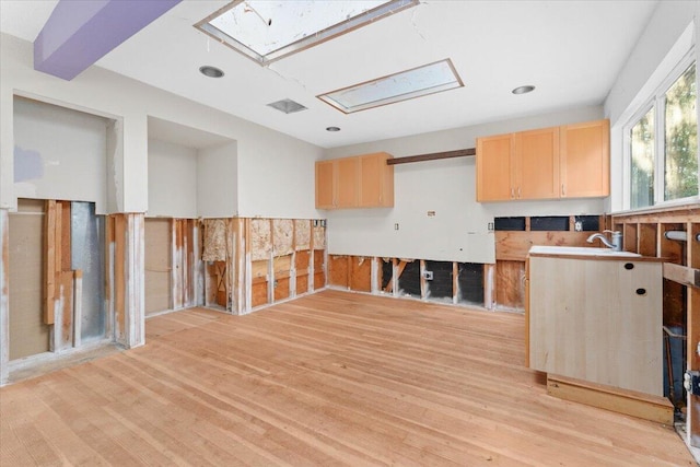 unfurnished room with light wood finished floors, a skylight, and a sink