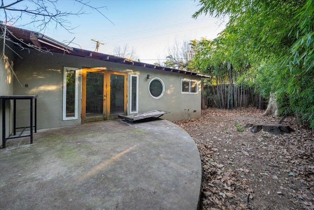 rear view of property featuring french doors, a patio area, fence, and stucco siding