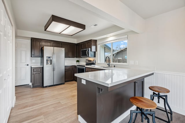 kitchen featuring appliances with stainless steel finishes, a peninsula, light countertops, a kitchen bar, and a sink