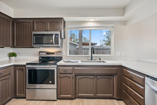 kitchen featuring light countertops, appliances with stainless steel finishes, a sink, and dark brown cabinets