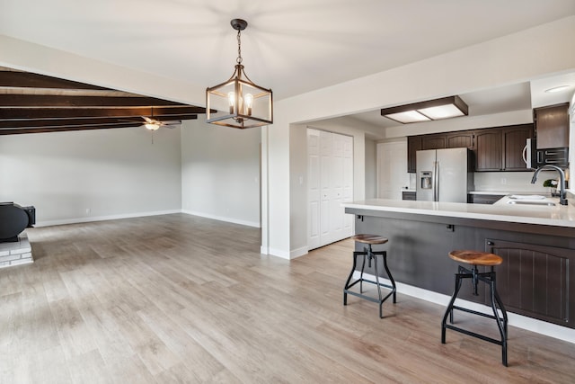 kitchen with stainless steel appliances, a peninsula, a sink, dark brown cabinets, and light countertops