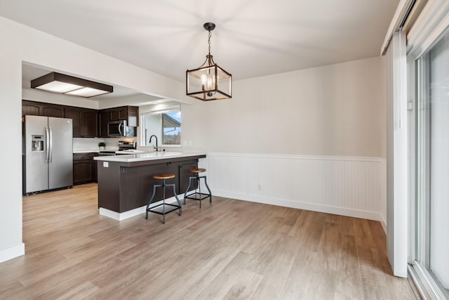 kitchen with decorative light fixtures, a peninsula, stainless steel appliances, dark brown cabinets, and light countertops