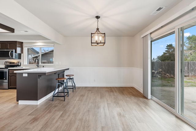 kitchen featuring appliances with stainless steel finishes, a breakfast bar, light countertops, dark brown cabinets, and pendant lighting