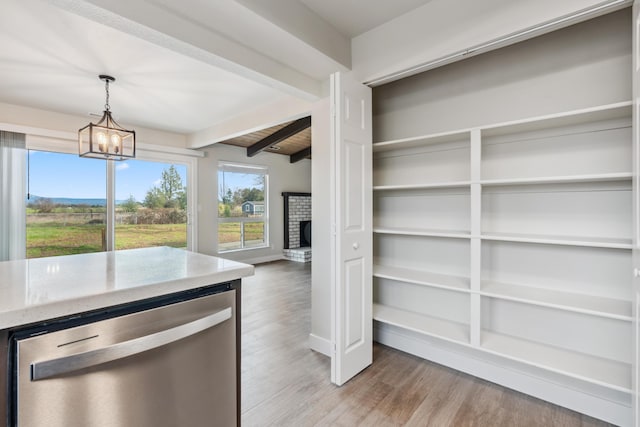 interior space with wood finished floors, light countertops, stainless steel dishwasher, beamed ceiling, and decorative light fixtures