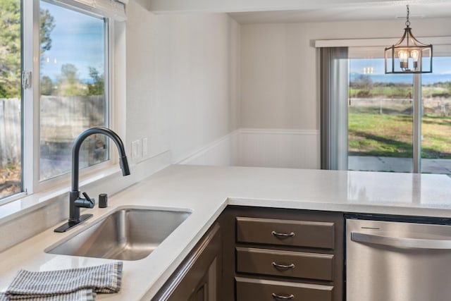 kitchen with light countertops, stainless steel dishwasher, a sink, and decorative light fixtures