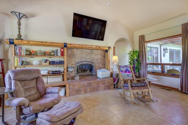 living room featuring visible vents, vaulted ceiling, a tiled fireplace, and light tile patterned flooring