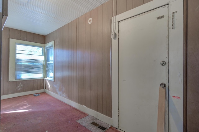 unfurnished room featuring wood walls, light colored carpet, visible vents, and baseboards