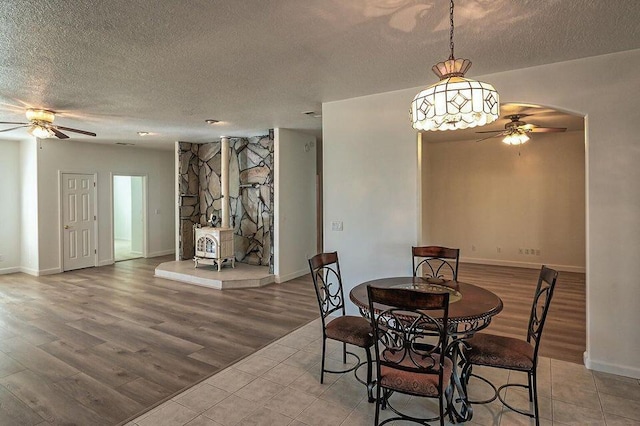 dining area featuring light wood-style floors, a textured ceiling, arched walkways, and a ceiling fan