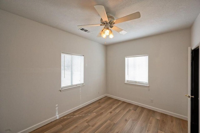 spare room featuring plenty of natural light, wood finished floors, visible vents, and baseboards