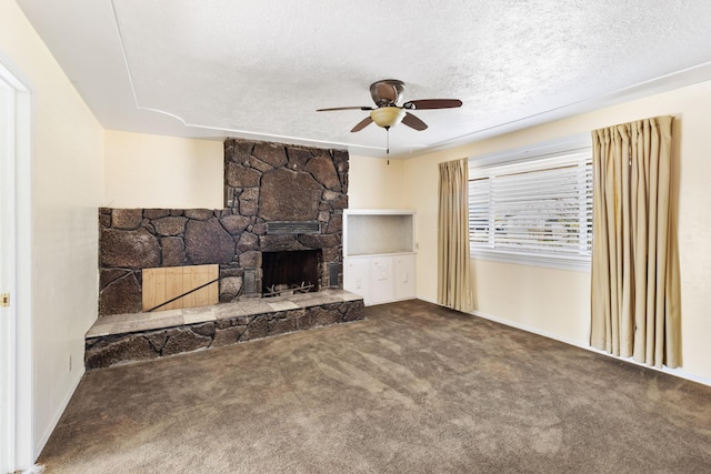 unfurnished living room featuring a textured ceiling, ceiling fan, a stone fireplace, and carpet flooring