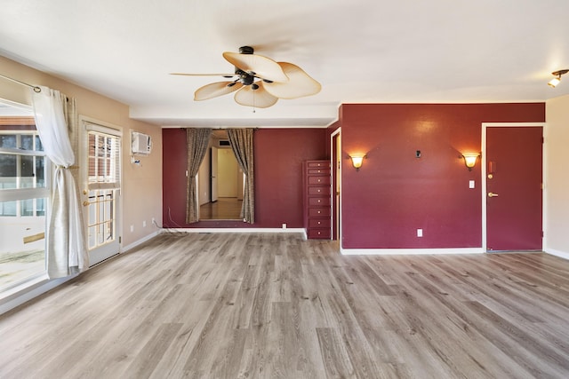 unfurnished living room with light wood finished floors, a ceiling fan, baseboards, and an AC wall unit