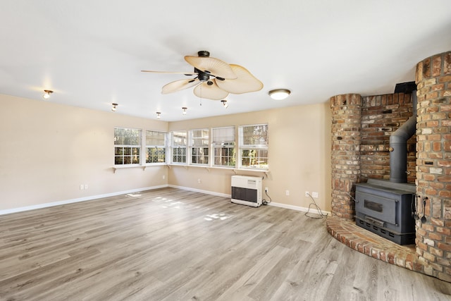 unfurnished living room featuring heating unit, light wood-style flooring, a ceiling fan, a wood stove, and baseboards