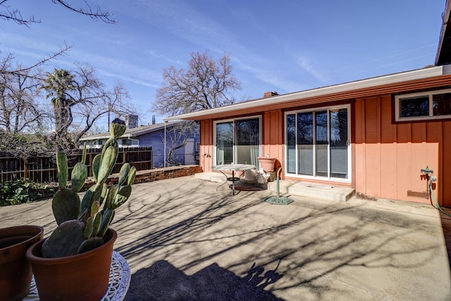 rear view of property with board and batten siding, a patio area, fence, and a chimney