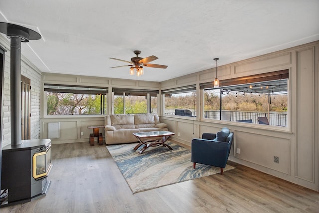 sunroom / solarium featuring a ceiling fan, a wood stove, and a healthy amount of sunlight