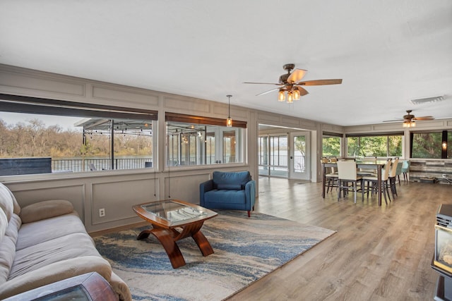 living area with light wood-style floors, visible vents, a decorative wall, and ceiling fan