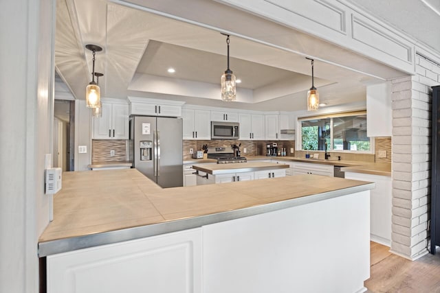 kitchen with stainless steel appliances, a raised ceiling, and white cabinets